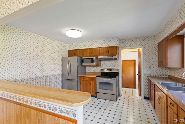 299 Sharp Rd, Granby, NY 13069 - kitchen featuring stainless steel appliances, wallpapered walls, a sink, under cabinet range hood, and brown cabinets
