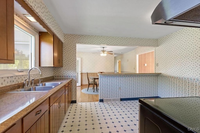 299 Sharp Rd, Granby, NY 13069 - kitchen with wallpapered walls, a sink, brown cabinetry, ceiling fan, and wall chimney range hood