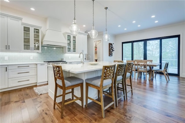 101 Coventry Rdg, Pittsford, NY 14534 - kitchen featuring custom exhaust hood, a kitchen bar, an island with sink, wood-type flooring, and tasteful backsplash