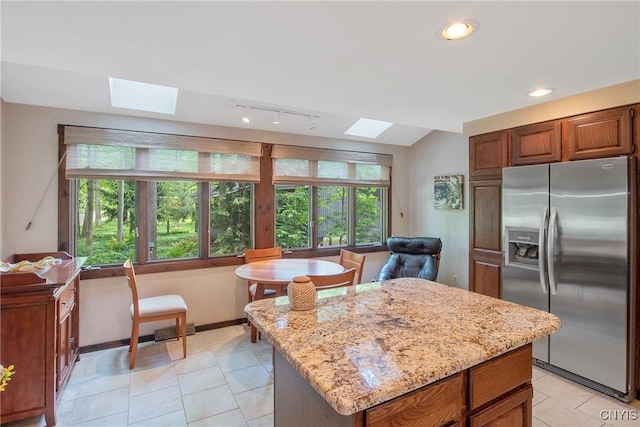8807 Wandering Way, Lysander, NY 13027 - kitchen with stainless steel fridge, a skylight, light stone counters, light tile patterned floors, and a center island