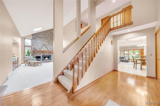 6157 Walnut Creek Ct, Clarence, NY 14051 - stairs with high vaulted ceiling, hardwood / wood-style flooring, a stone fireplace, baseboards, and a chandelier