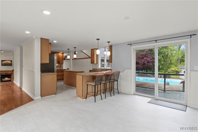 60 Gaylord Ct, Elma, NY 14059 - kitchen featuring brown cabinetry, a peninsula, a kitchen bar, hanging light fixtures, and a lit fireplace