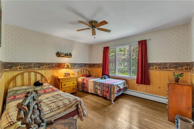 63 Lakeview Dr N, Middlefield, NY 13326 - bedroom with baseboard heating, wallpapered walls, wainscoting, hardwood / wood-style flooring, and ceiling fan