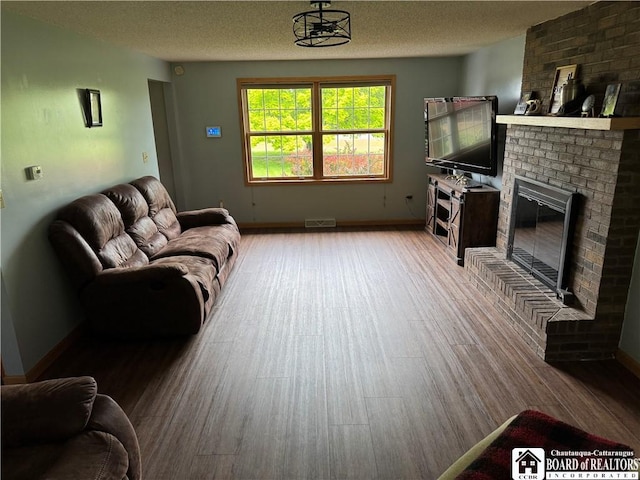 8900 Brownell Rd, Clymer, NY 14724 - living room featuring a brick fireplace, a textured ceiling, light wood-type flooring, and baseboards