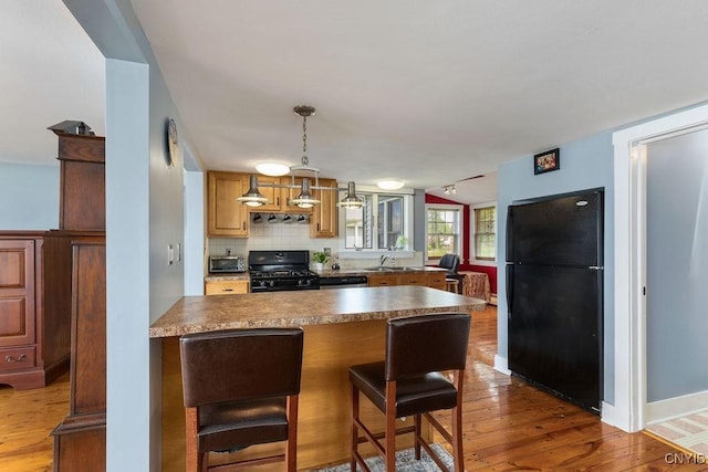 7649 Tuttle Rd, Cicero, NY 13030 - kitchen with black appliances, wood finished floors, decorative light fixtures, a breakfast bar, and a sink