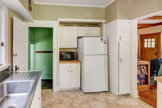 1031 Main St, Middletown, NY 12455 - kitchen with freestanding refrigerator, black microwave, a sink, white cabinets, and ornamental molding
