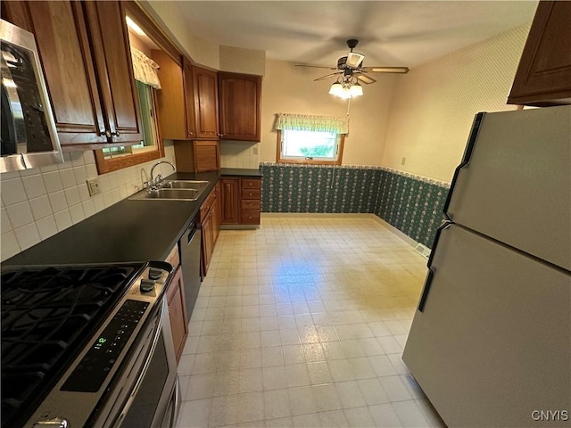 9385 Wickham Dr, Cicero, NY 13029 - kitchen featuring stainless steel appliances, a sink, dark countertops, ceiling fan, and a wainscoted wall