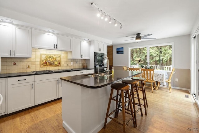 4962 Tall Oaks Dr, Manlius, NY 13066 - kitchen featuring dark countertops, a kitchen breakfast bar, decorative backsplash, light wood-style flooring, and white cabinets