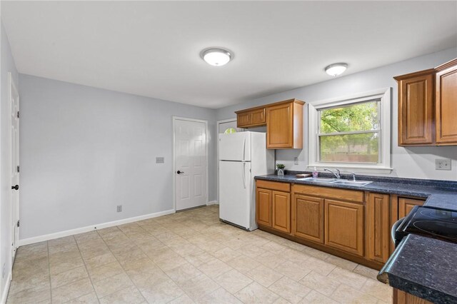 2200 W Henrietta Rd, Brighton, NY 14623 - kitchen featuring freestanding refrigerator, dark countertops, a sink, brown cabinetry, and baseboards