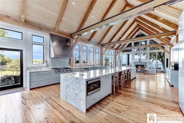 6007 Tinkertown Dr, Chautauqua, NY 14728 - kitchen featuring stainless steel microwave, wall chimney exhaust hood, gray cabinetry, light stone countertops, and high vaulted ceiling