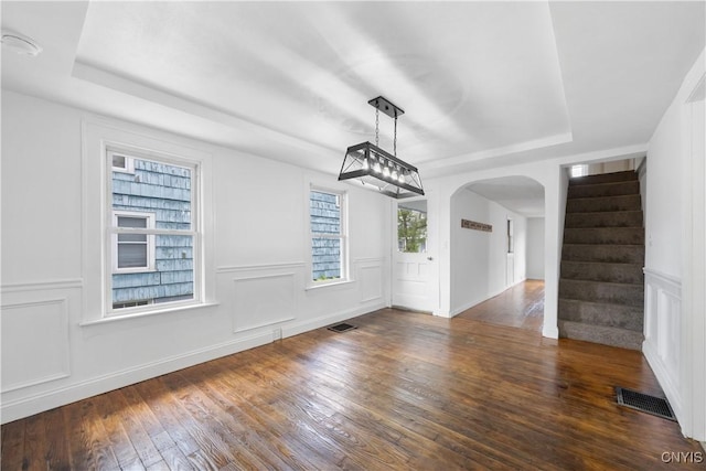 220 W Elm St, Oneida-Inside, NY 13421 - unfurnished dining area featuring a tray ceiling, arched walkways, wood finished floors, stairway, and a decorative wall