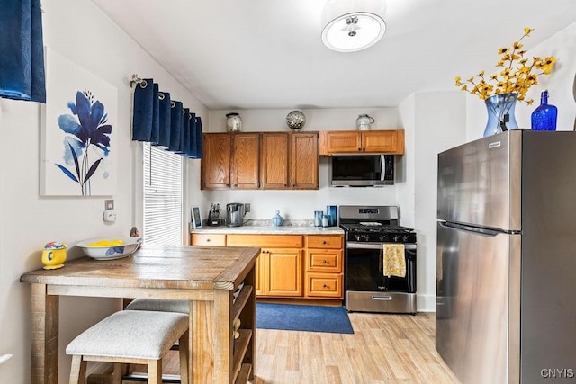 173 Mosley Dr Unit 1, Syracuse, NY 13206 - kitchen featuring appliances with stainless steel finishes, light wood finished floors, brown cabinetry, and a kitchen breakfast bar