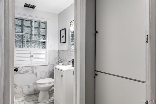 296 Burke Dr, Cheektowaga, NY 14215 - bathroom with marble look tiles, vanity, tile walls, toilet, and a wainscoted wall