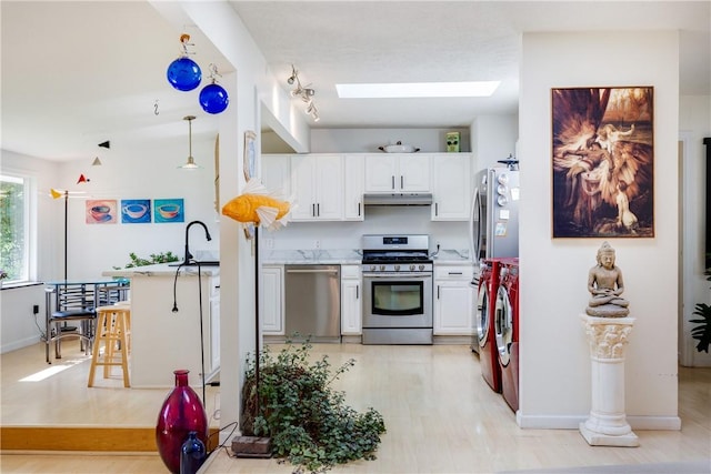 2804 Westinghouse Rd, Horseheads, NY 14845 - kitchen with appliances with stainless steel finishes, washing machine and dryer, a skylight, under cabinet range hood, and white cabinetry