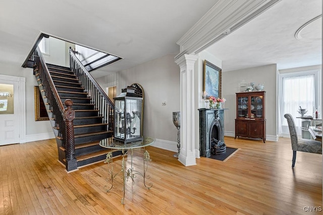 54 W 5th St, Oswego-City, NY 13126 - staircase featuring hardwood / wood-style floors, baseboards, a fireplace with flush hearth, and decorative columns