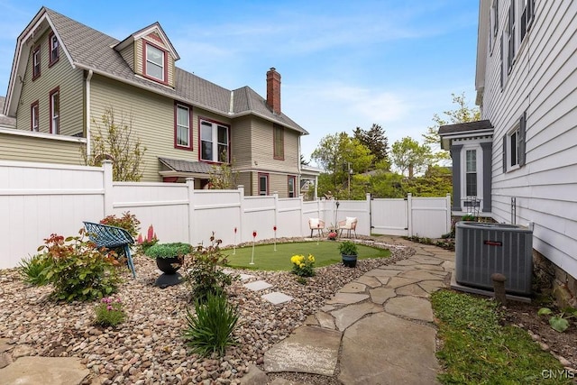 54 W 5th St, Oswego-City, NY 13126 - view of home's exterior with a putting area, central air condition unit, a chimney, a fenced backyard, and roof with shingles