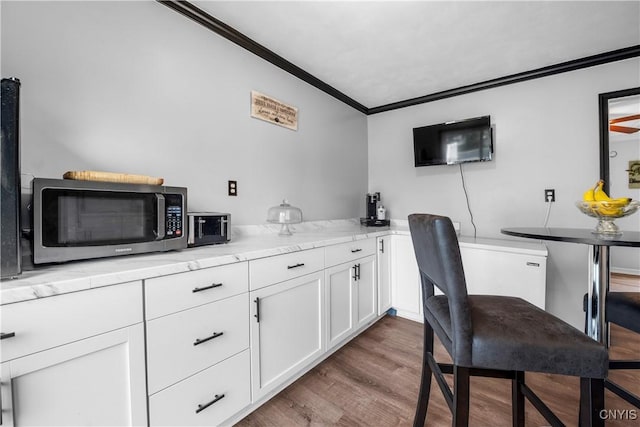 30 Bakeman St, Fulton, NY 13069 - kitchen with stainless steel microwave, ornamental molding, white cabinetry, and wood finished floors