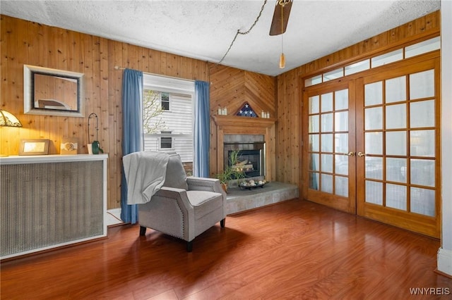2654 Main St, Newfane, NY 14108 - sitting room with radiator heating unit, a textured ceiling, french doors, wood walls, and a fireplace with raised hearth