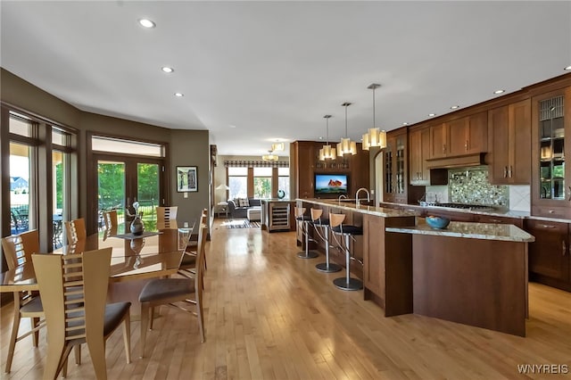 35 Pinegrove Ct, Elma, NY 14059 - kitchen with a kitchen island with sink, a kitchen bar, stainless steel gas cooktop, light wood finished floors, and glass insert cabinets