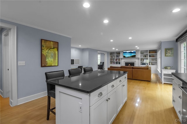 11 S Meadow Dr, Orchard Park, NY 14127 - kitchen with dark countertops, a breakfast bar, white cabinetry, a warm lit fireplace, and light wood-type flooring