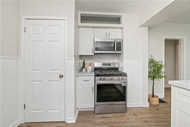 131 Pomona Dr, Greece, NY 14616 - kitchen with stainless steel appliances, white cabinetry, a wainscoted wall, light wood-type flooring, and light countertops