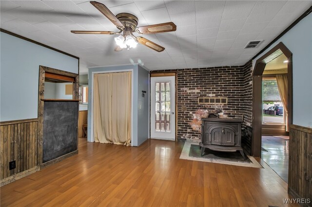 6305 E Main St, Byron, NY 14557 - unfurnished living room featuring ceiling fan, a wood stove, a wainscoted wall, wood finished floors, and wood walls