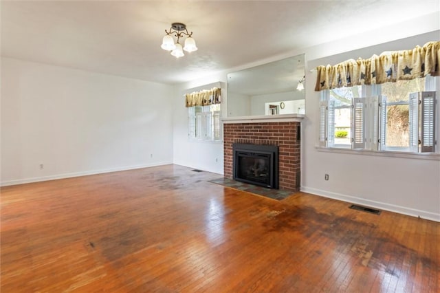 4411 Williamson Rd, Marion, NY 14505 - unfurnished living room featuring wood-type flooring, a chandelier, a brick fireplace, and baseboards