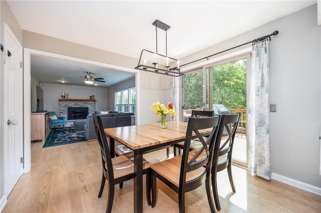 6 Barben Cir, Mendon, NY 14506 - dining room featuring light wood-type flooring, a chandelier, a stone fireplace, ceiling fan, and baseboards