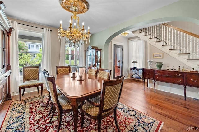 55 E 5th St, Oswego-City, NY 13126 - dining room featuring arched walkways, wood-type flooring, a chandelier, and stairs