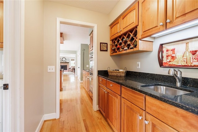 74 Broadmoor Trl, Perinton, NY 14450 - kitchen with a sink, light wood-style flooring, dark stone counters, baseboards, and brown cabinets