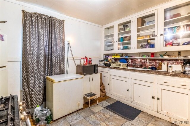 110 10th St, Buffalo, NY 14201 - kitchen with black microwave, white refrigerator, white cabinetry, glass insert cabinets, and light stone finish floors