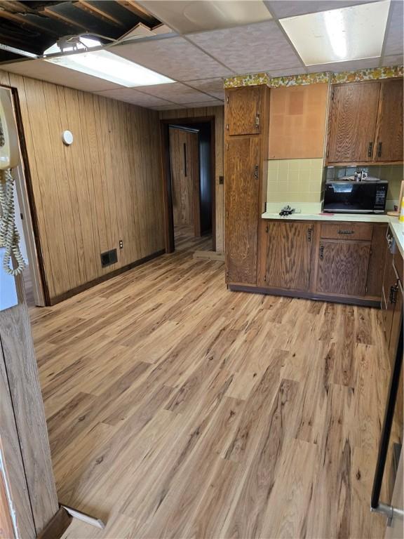 95 Wadsworth Ave, Avon, NY 14414 - kitchen with black microwave, light wood-style floors, light countertops, brown cabinetry, and wood walls
