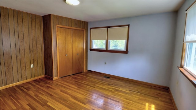 6251 Willard St, Aurelius, NY 13034 - unfurnished bedroom with wood finished floors, a closet, multiple windows, wood walls, and baseboards
