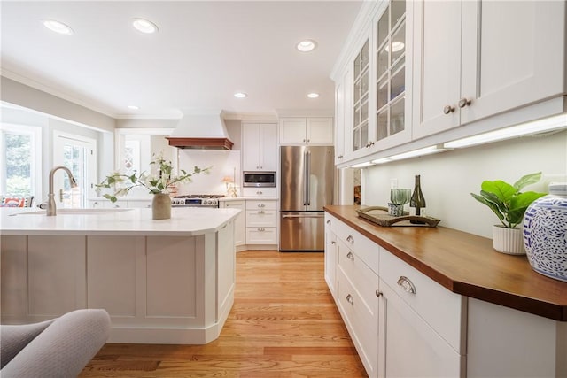 307 Allens Creek Rd, Brighton, NY 14618 - kitchen featuring appliances with stainless steel finishes, wall chimney range hood, a sink, wooden counters, and light wood-style floors