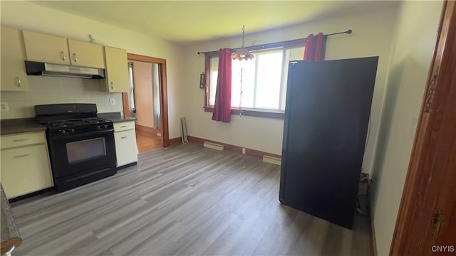 1324 Butternut St, Utica, NY 13502 - kitchen with black gas stove, under cabinet range hood, light wood-style floors, cream cabinets, and tasteful backsplash