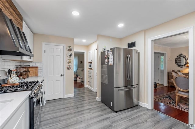 101 Doll Pkwy, Syracuse, NY 13214 - kitchen with appliances with stainless steel finishes, wall chimney exhaust hood, light wood finished floors, light countertops, and white cabinets