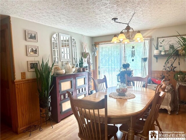 9983 Deer Creek Rd, Genesee, NY 14770 - dining space featuring a chandelier, a textured ceiling, light wood-style floors, wainscoting, and wooden walls