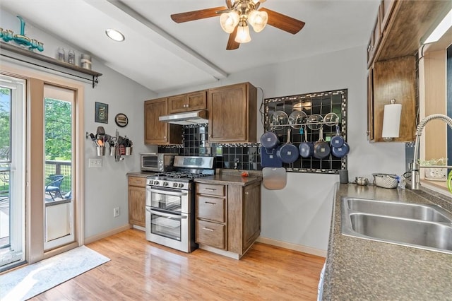 13385 Seneca St, Savannah, NY 13146 - kitchen featuring range with two ovens, a sink, under cabinet range hood, brown cabinetry, and backsplash