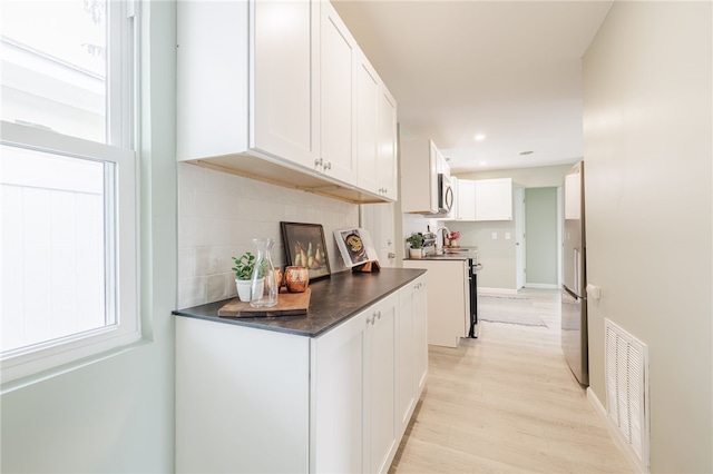 237 Heberle Rd, Irondequoit, NY 14609 - kitchen with dark countertops, appliances with stainless steel finishes, white cabinetry, light wood finished floors, and decorative backsplash