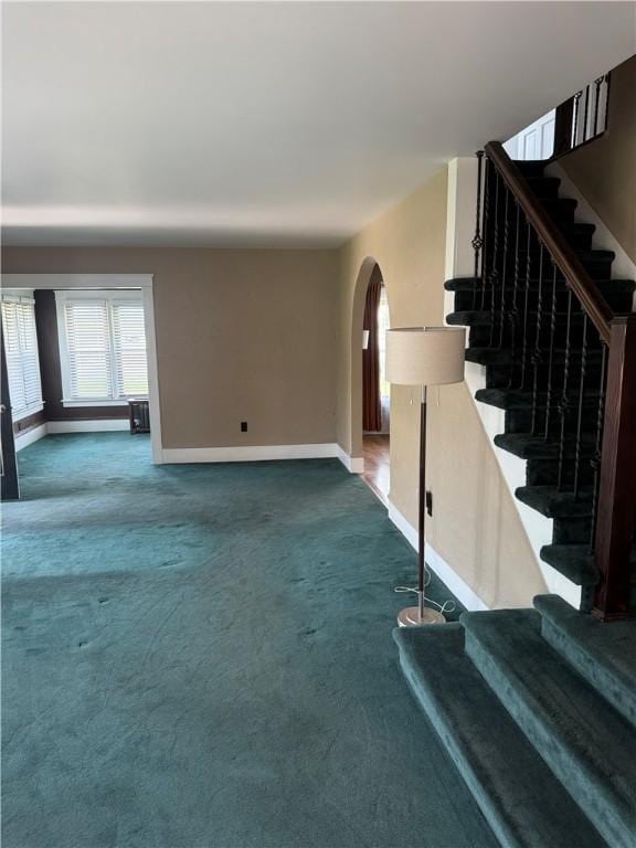 16 Cobbles E, Elmira, NY 14905 - unfurnished living room featuring baseboards, dark colored carpet, arched walkways, and stairs