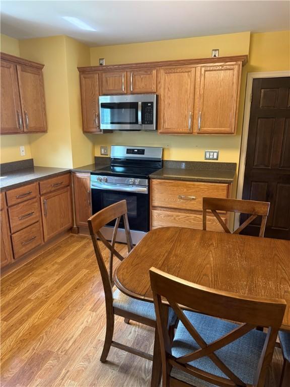 16 Cobbles E, Elmira, NY 14905 - kitchen featuring stainless steel appliances, light wood-style flooring, dark countertops, and brown cabinetry