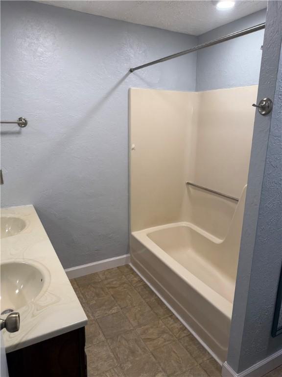 16 Cobbles E, Elmira, NY 14905 - full bath with double vanity, shower / washtub combination, a textured wall, and baseboards