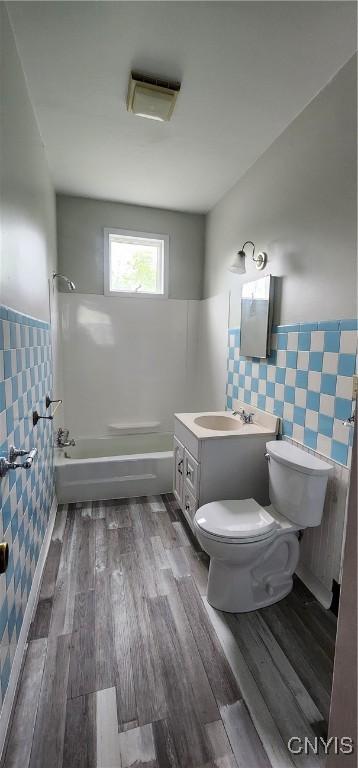 16 Bryant St, Utica, NY 13502 - full bath featuring toilet, wainscoting, tile walls, washtub / shower combination, and wood finished floors