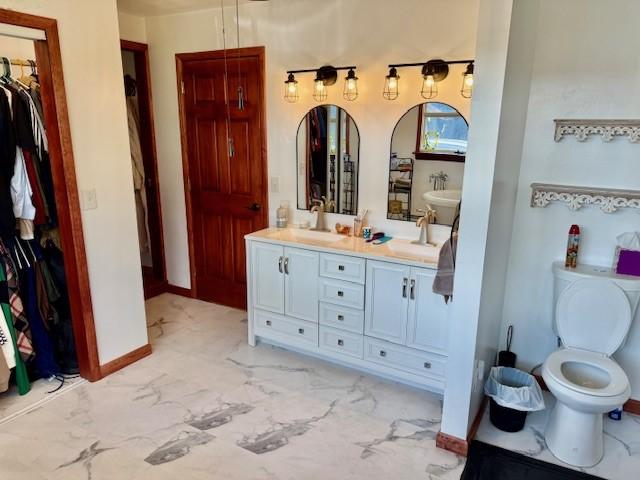 251 Pearsall Rd, Westford, NY 12155 - full bathroom featuring double vanity, marble look tile flooring, a walk in closet, baseboards, and toilet