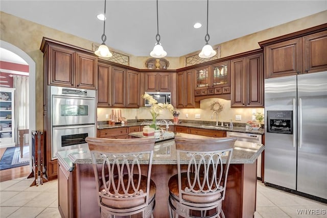 81 Hidden Oaks Ct, Grand Island, NY 14072 - kitchen with stainless steel appliances, a sink, light tile patterned flooring, arched walkways, and a kitchen island with sink