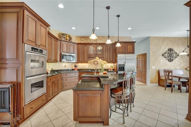 81 Hidden Oaks Ct, Grand Island, NY 14072 - kitchen featuring appliances with stainless steel finishes, brown cabinets, light tile patterned floors, a breakfast bar area, and recessed lighting