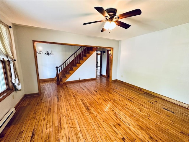 6956 E Washington St, Bath, NY 14810 - empty room with a baseboard heating unit, wood-type flooring, stairs, a ceiling fan, and baseboards