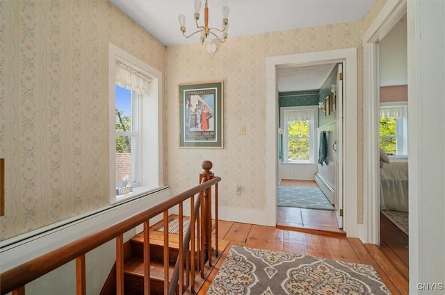 8796 State Highway 12, Sherburne, NY 13460 - corridor with hardwood / wood-style flooring, a chandelier, an upstairs landing, a baseboard radiator, and wallpapered walls