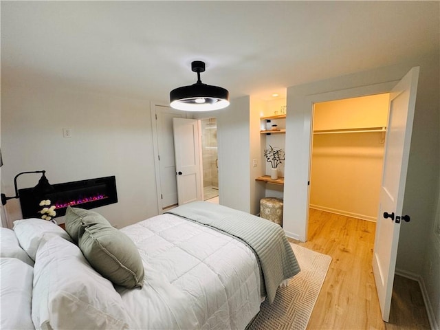 11 Laureldale Dr, Pittsford, NY 14534 - bedroom featuring light wood-style flooring, a spacious closet, baseboards, and a glass covered fireplace