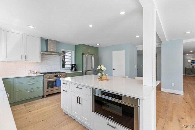 3 Elson Ln, Skaneateles, NY 13152 - kitchen with high end appliances, wall chimney exhaust hood, green cabinets, light countertops, and light wood-style flooring